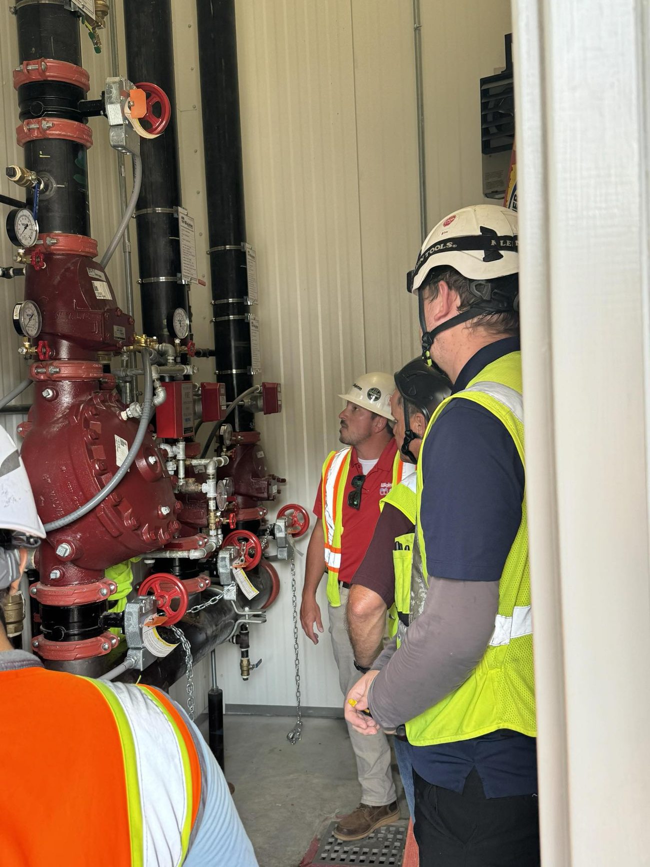 Wiginton technicians in hard hats and high-visibility vests in a sprinkler riser room
